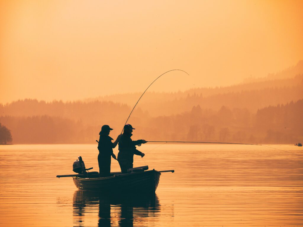 Silhouette of man fishing on lake from boat at sunset